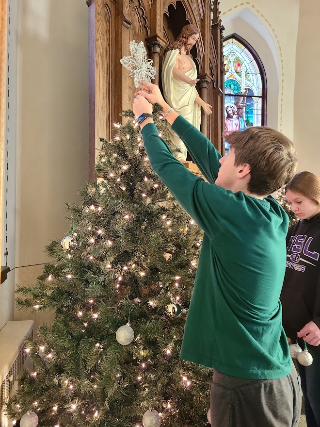 teenage boy placing a star on the top of the Christmas tree